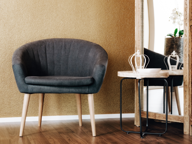 Grauer Polstersessel neben einem kleinen Beistelltisch mit Dekoration vor einem goldfarbenen Wandhintergrund